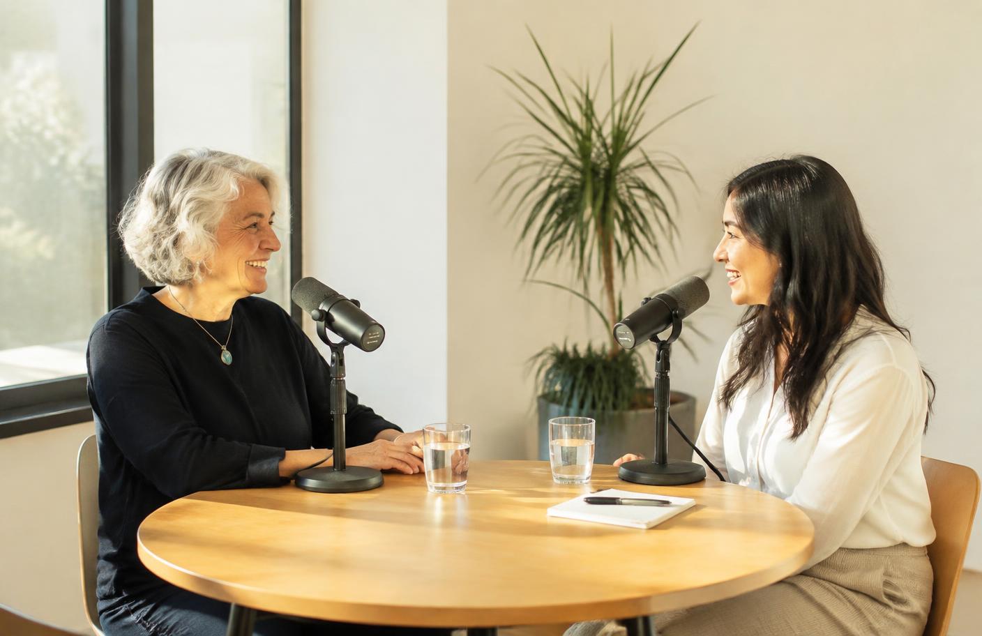 Two people in conversation at a table with microphones in a bright room